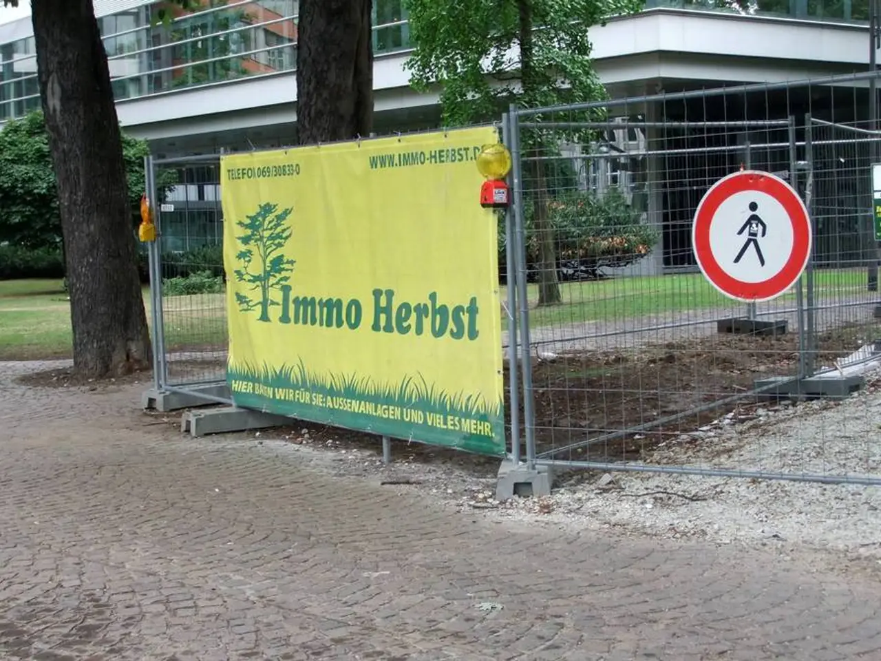 In this image there is a fence having few boards and a banner are attached to it. Left side there...