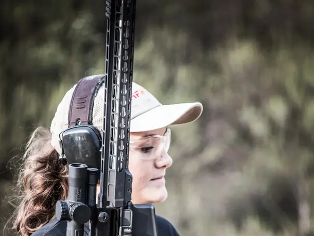 In this image, there is a person on the blur background. This person is holding a gun with her...