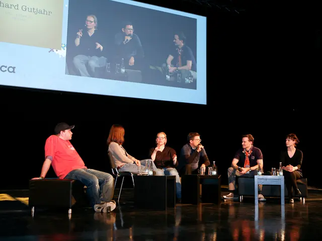 Six persons are sitting on the sofa and chairs and in the middle these two persons are talking...