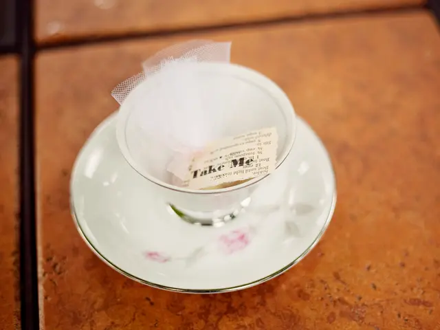 In this image we can see a cup containing a paper with text and net is placed on the saucer kept on...