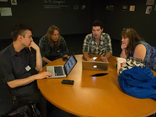 in this image there are four people who are working on a laptop. To the left side there is a man...